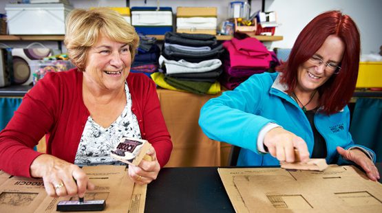 Two women stamping cardboard to be used as packaging.
