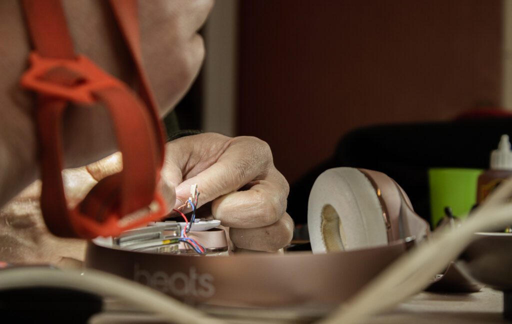 Close up image of a hand repairing headphones on a table.