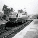 Black and white picture of a train on the track at a railway station.
